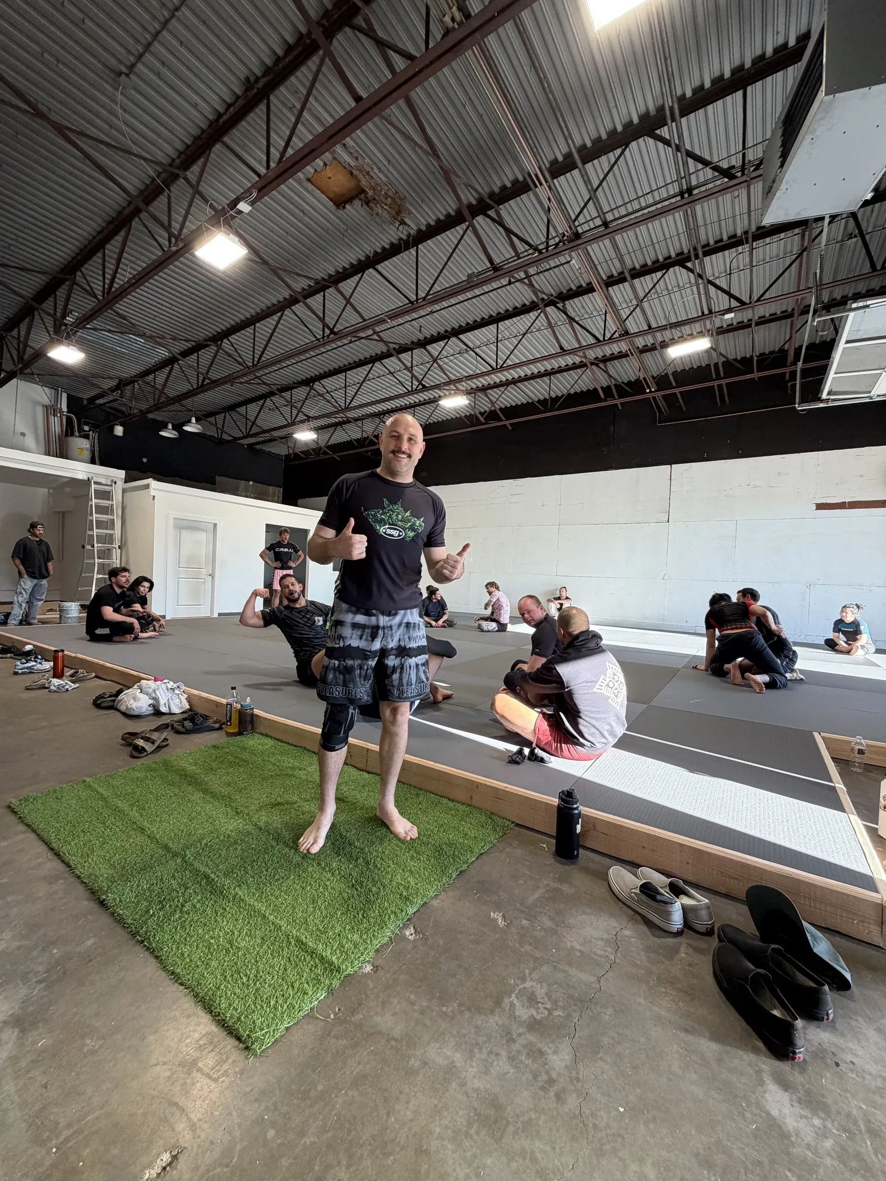 Coach smiling on the mats between rounds at Neighborhood Jiu Jitsu.